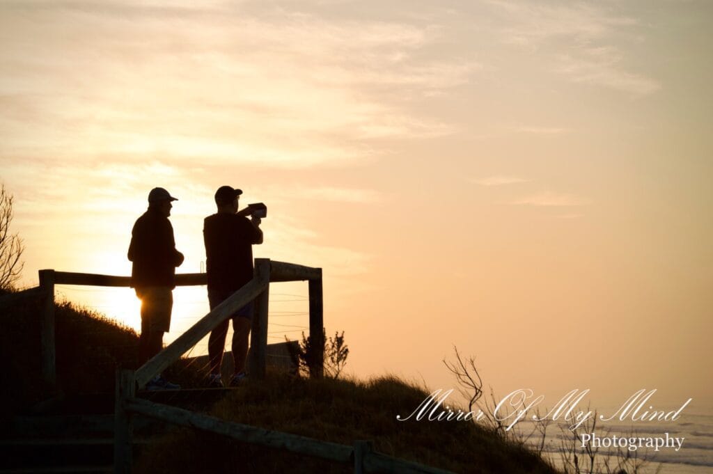 Two people silhouetted at coastal lookout during sunrise in Australia