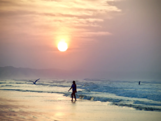 A lone swimmer walks along the shoreline at Ocean Grove during sunrise with soft waves and warm morning light.