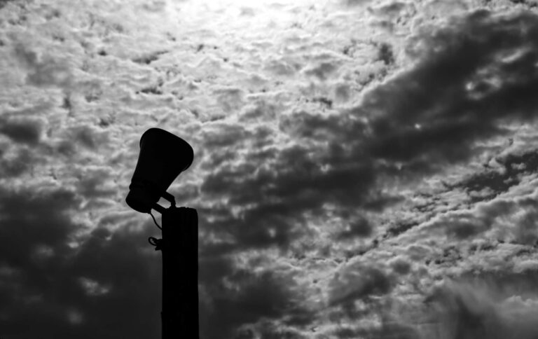Silhouette of a lone loudspeaker on a pole against a dramatic cloud-filled sky in Ocean Grove.