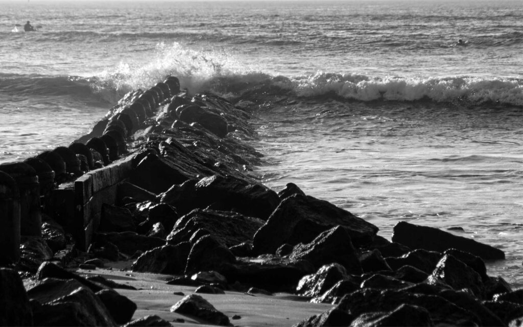 Black-and-white seascape of Point Lonsdale where waves crash against a rocky seawall, highlighted by textured stones leading to the horizon.